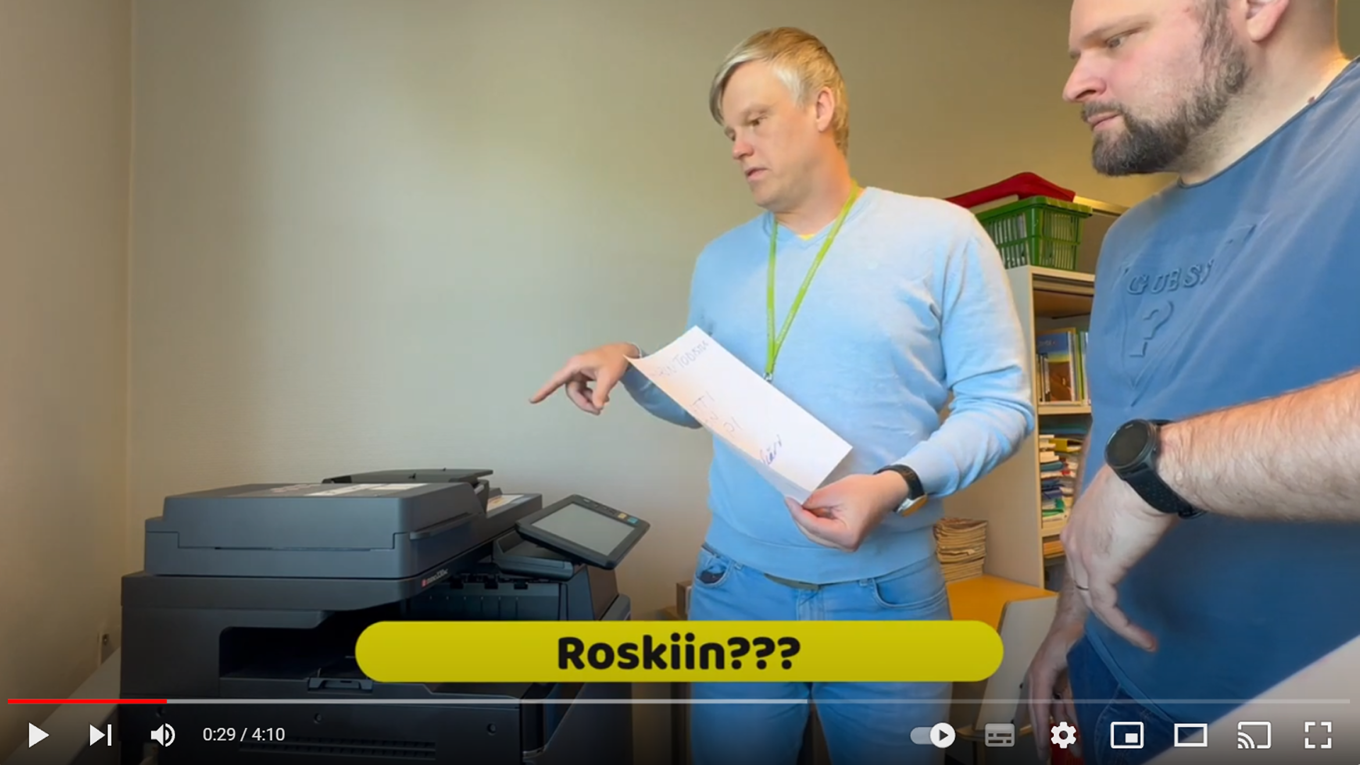 Kaksi opettajaa tulostimen äärellä YouTube-videolla.